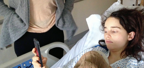 Emilia Clarke lying in her hospital bed and using her phone