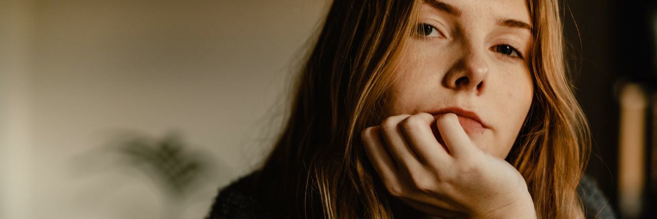 Why You Shouldn't Say Something Makes You Anxious photo of young woman resting chin on hand and looking into camera with stern expression