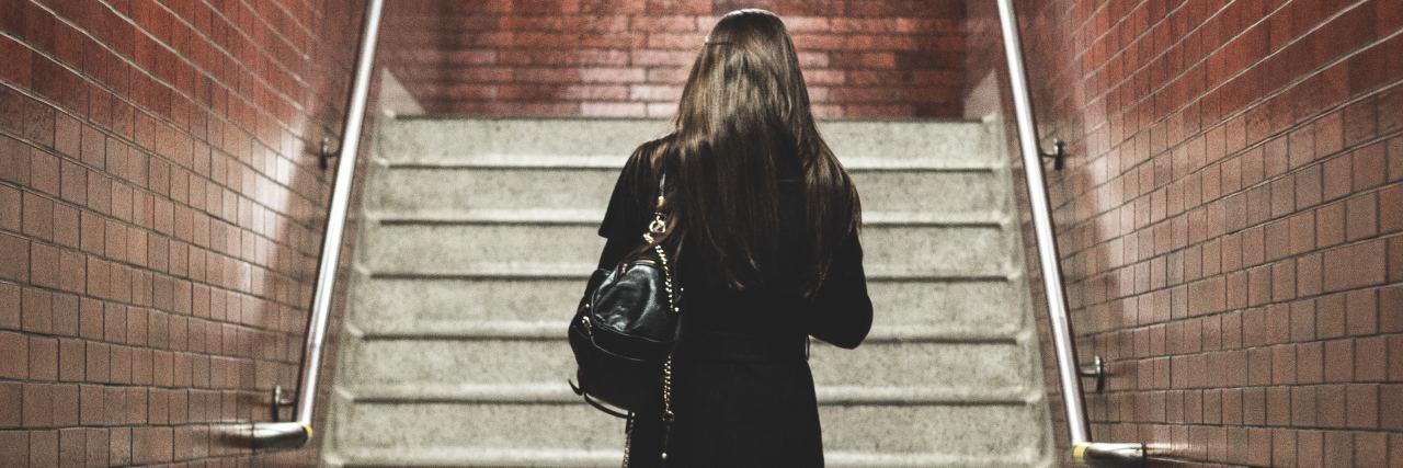 photo of woman alone about to climb stairs in subway