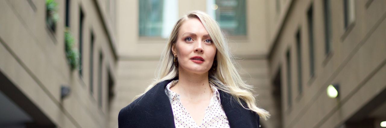 What to Know About ‘Emotional Hypervigilance’ portrait photo of blonde woman looking upset with buildings behind her