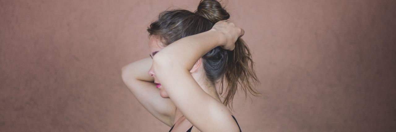 What It's Like to Be a Teenager With POTS A woman with her hair up, her face covered by her arm, looking to the side