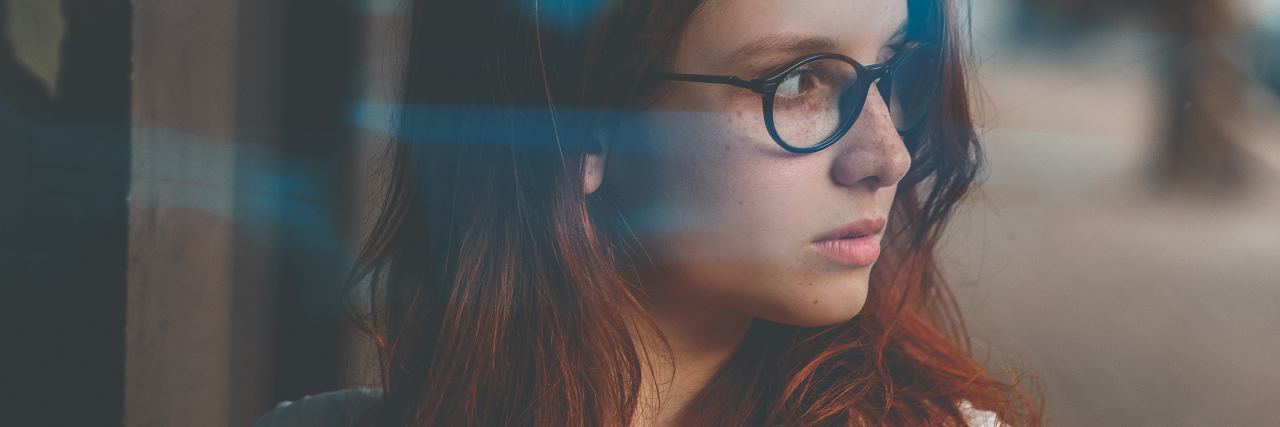Symptoms I Struggle With as an Adult With ADHD photo of young woman wearing glasses and looking off-camera at something unseen.