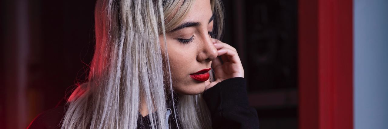 photo of young light blonde woman with eyes closed in room with red walls