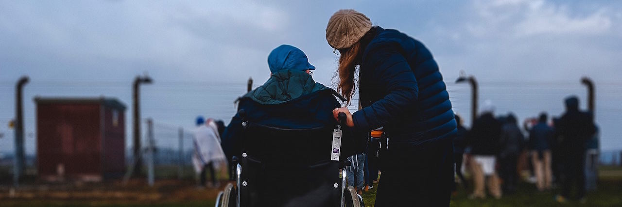 A woman in a wheelchair sitting next to an ablebodied woman. They're watching a baseball game, it's dusk.