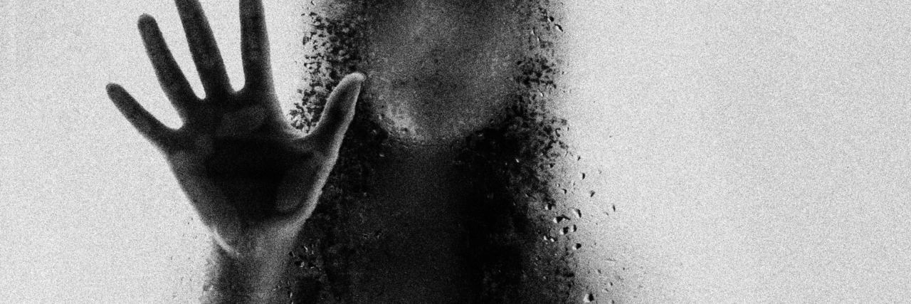 black and white photo of woman behind frosted glass with most of face blurred and hand raised to touch glass