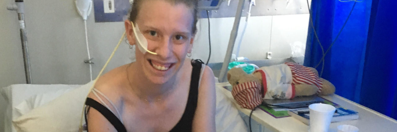 Why I Need a Feeding Tube in Anorexia Recovery photo of contributor, a young woman on a hospital bed with a feeding tube through her nose and a large golden labrador dog on the bed with her