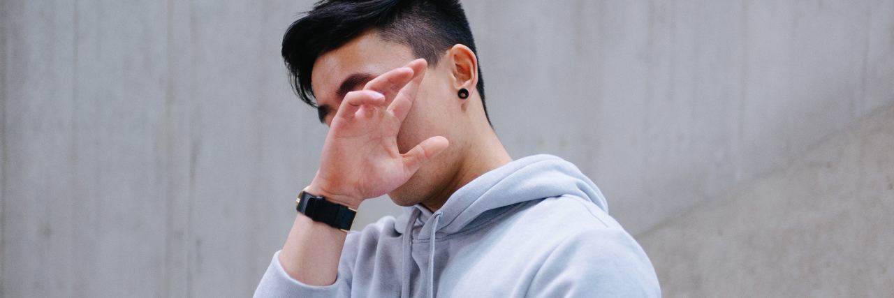 young asian teen man hiding his face with his hand and turning away