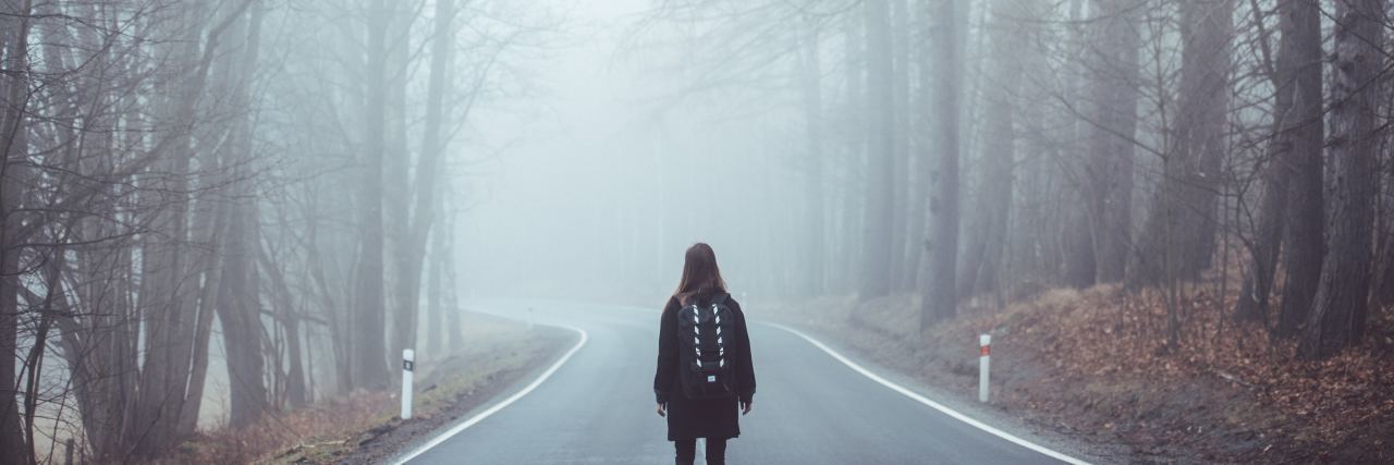 woman standing in road in the middle of foggy woods