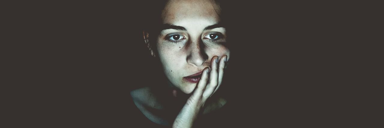 Taking Time Alone in My Hotel Room for My Mental Health When Traveling photo of woman lit by screen resting face on hand in dark room