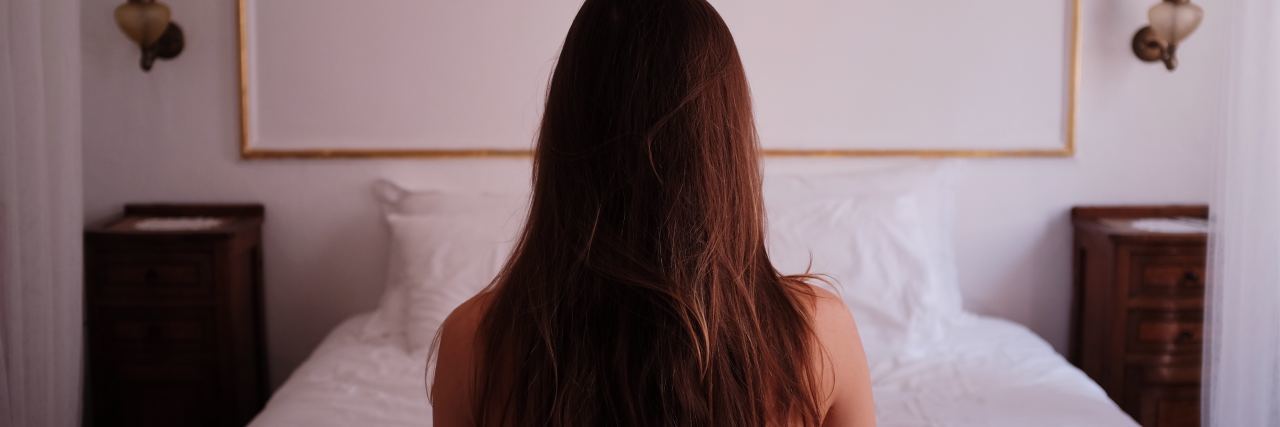 photo of woman with back to camera sitting on bed in silence