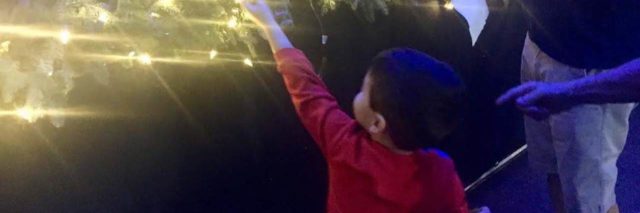 Little boy reaching up to get a piece of paper at a holiday event