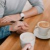 close up photo of two people holding hands while having coffee
