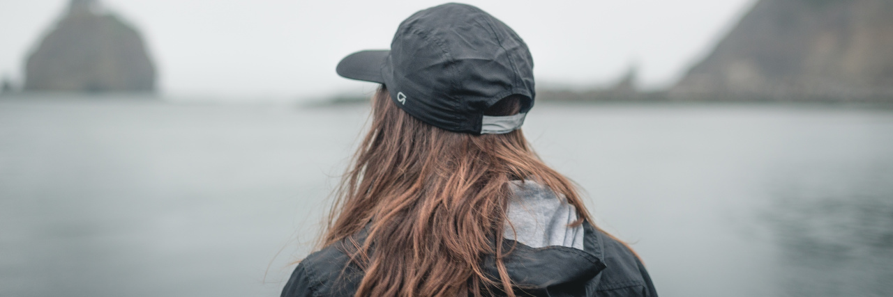 photo of woman wearing baseball cap looking away from camera and staring out at foggy sea horizon