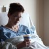 photo of female patient with short hair sitting in hospital bed holding cup of soup