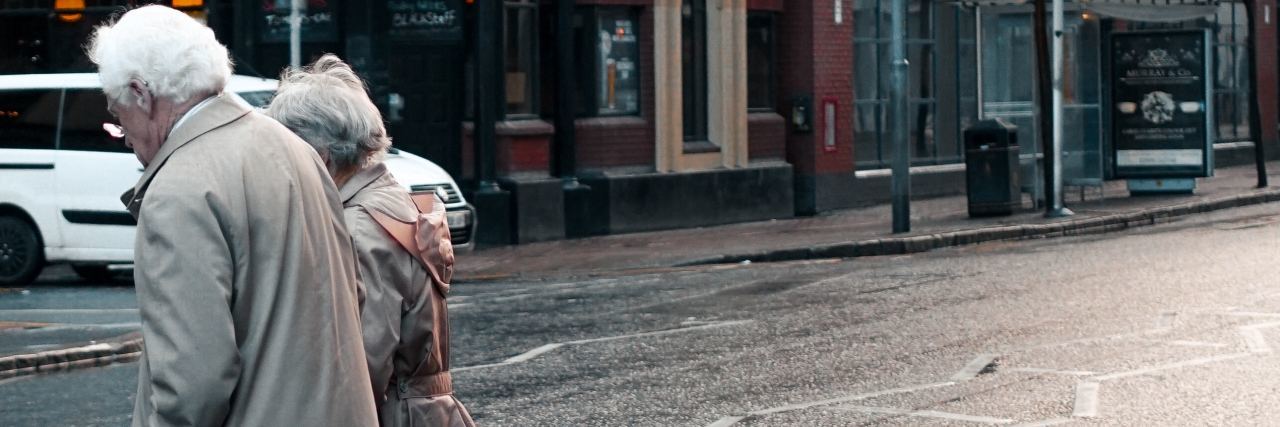 7 Tips on How to Manage Dementia Older couple walking closely together across a wet street in an urban area.