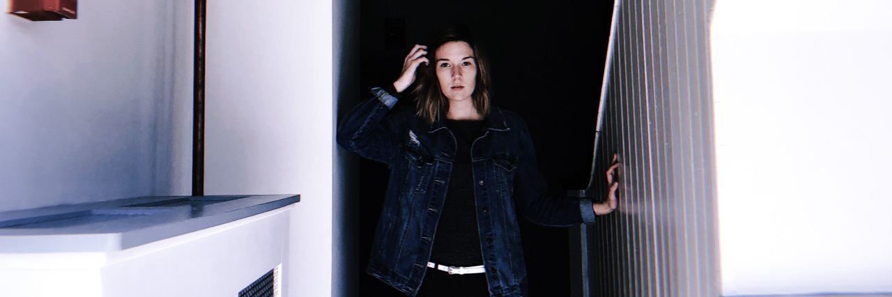 Pushing Your Comfort Zone With a Chronic Illness photo of woman standing in white hallway with darkness at end