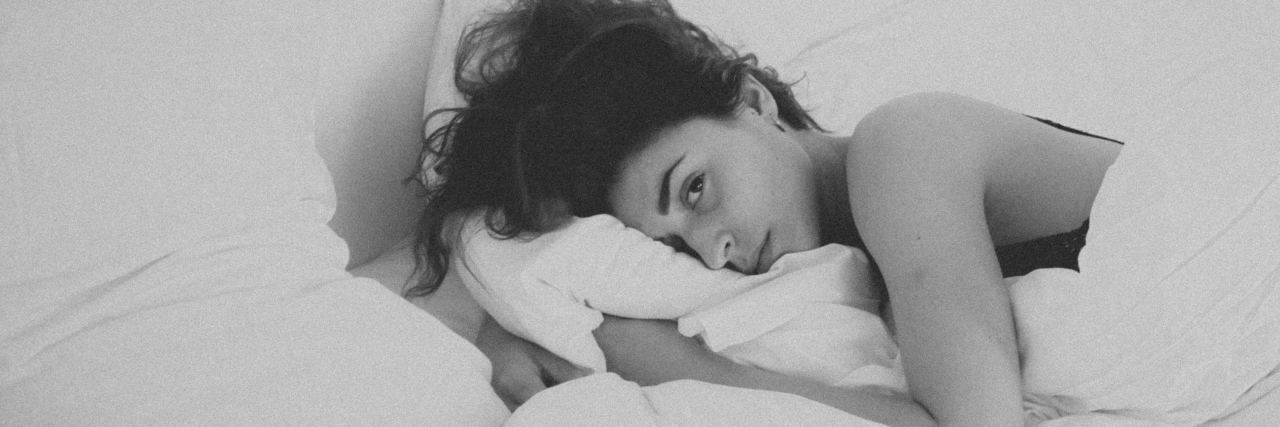 black and white photo of young woman in bed looking sad and looking at camera