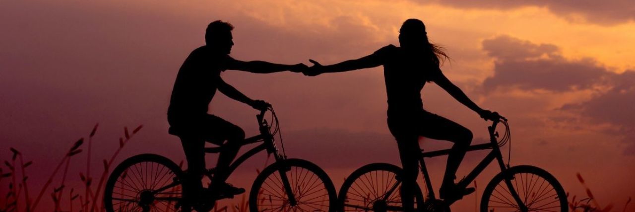 couple riding bikes holding hands sunset