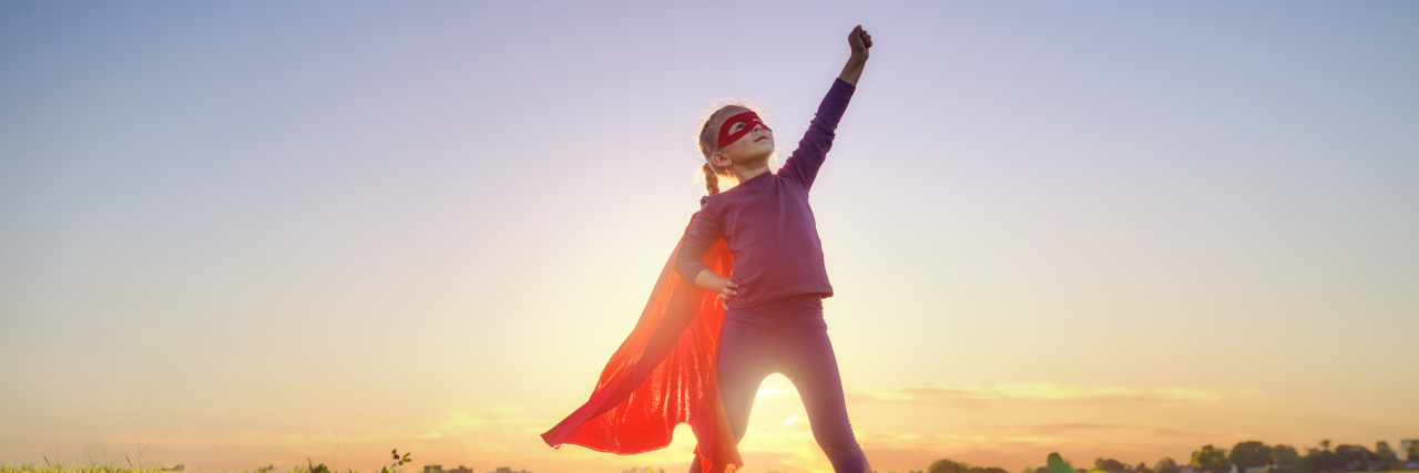 child wearing a superhero cape in a field