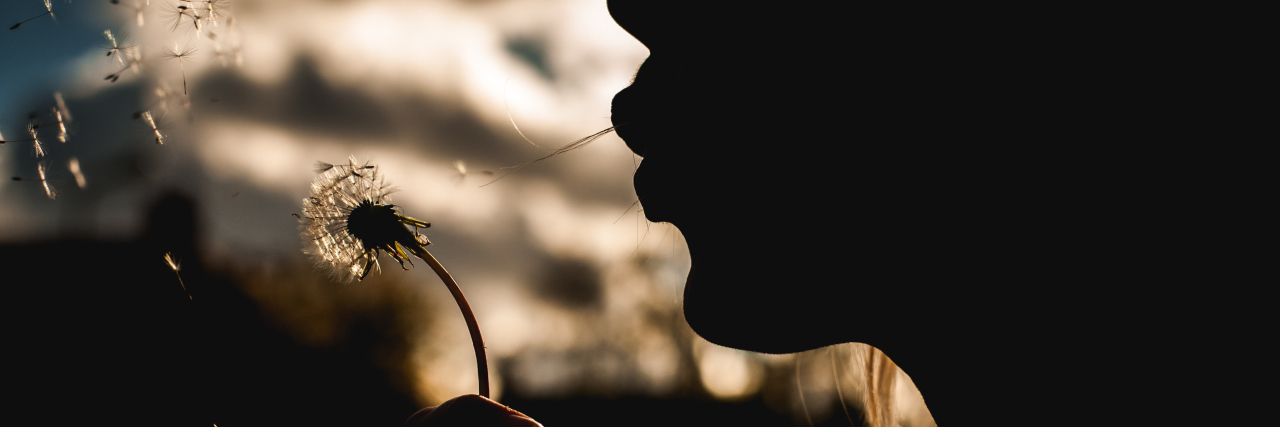 a silhouette of a girl blowing a dandelion