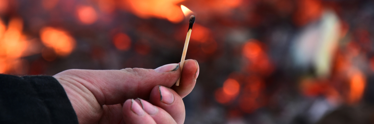 Inside the Mind of a Teen With Pyromania An image of a man's hand holding an open flame with a large fire in the background.