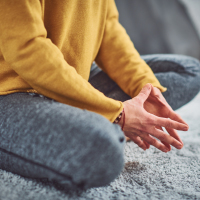 close up photo of woman sitting cross legged on floor in lotus pose with hands together