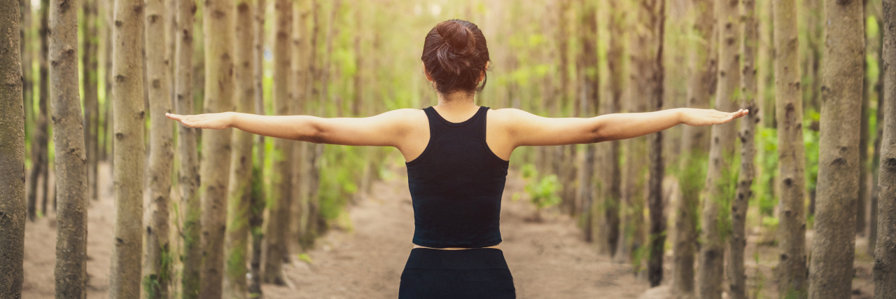 What Stability Feels Like After Bipolar Disorder a woman is spreading her arms in the forest