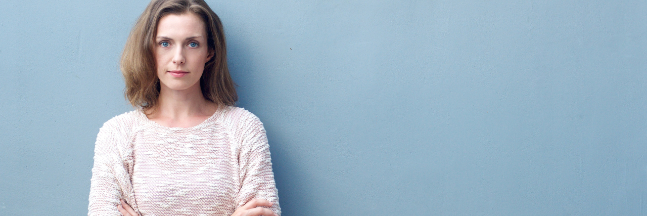 'Resting Pain Face' Is Part of My Chronically Ill Daily Life a woman is standing up against a wall with her arms folded