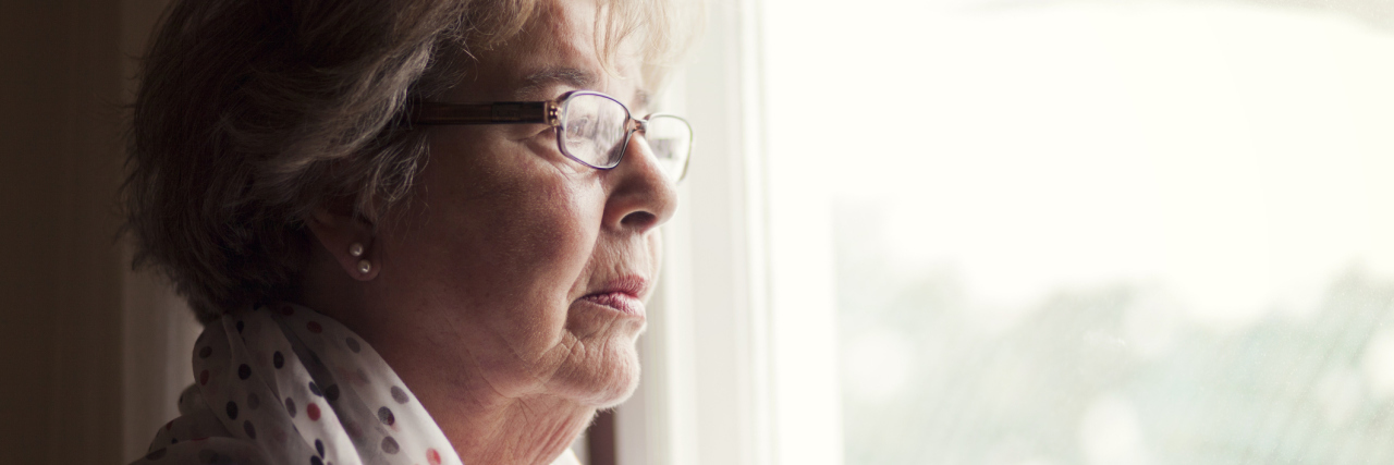 older woman wearing a robe and glasses and looking out the window