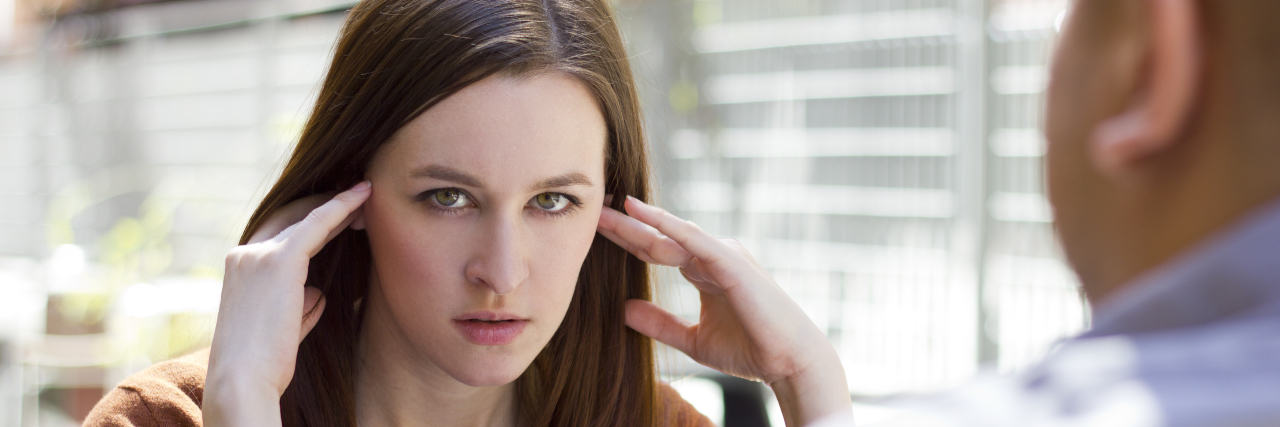 Why We Should Stop Using Chronic Illnesses as Hyperbole a woman sitting with a man at a table with her hands on her temples
