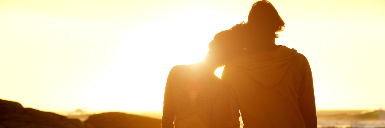 Portrait from behind of loving couple holding hands at the beach and watching the sunset