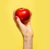 An apple in a hand over yellow background