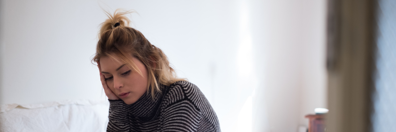 Dealing With Flare-Ups and Systemic Autoinflammatory Disease woman sitting on bed, looking tired