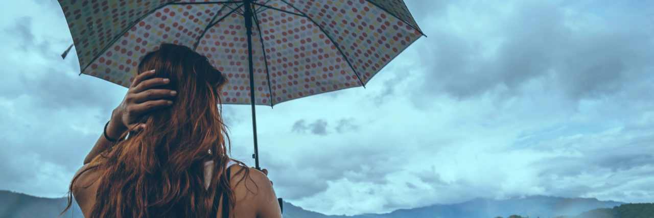 Working Through Self-Criticism With Chronic Pain Woman holding umbrella in a storm.