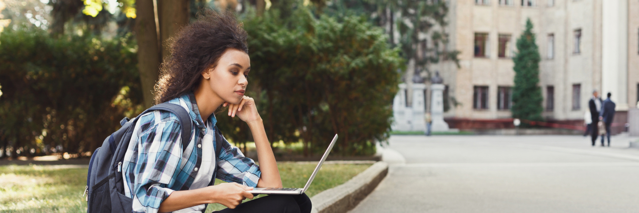Attending College With Pseudotumor Cerebri Student sitting on curb using laptop.