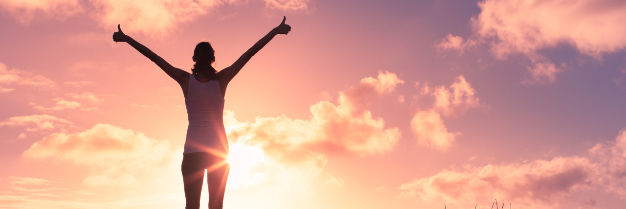 Being Called a 'Warrior' With Chronic Illness Young woman with arms in the air giving thumbs up.