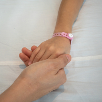 Parent holds the hand of a sick child in a hospital.
