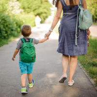 A woman walking with her son, who's wearing a backpack. They are holding hands.