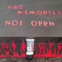 photo of black painted box with silver lock and painted red flames. On the top is written "bad memories, do not open"