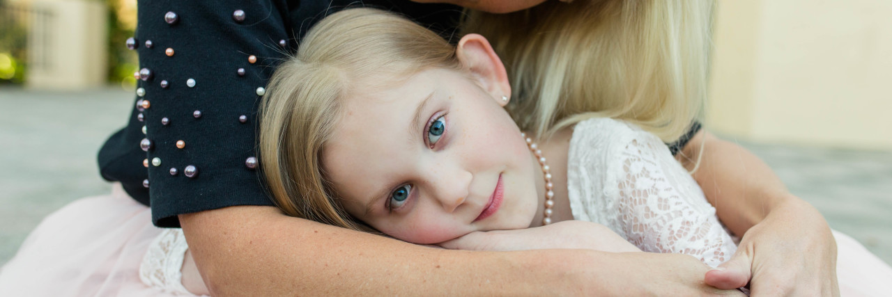 I Blamed Myself for My Daughter's Health Issues Mother hugging daughter who is resting on her lap.