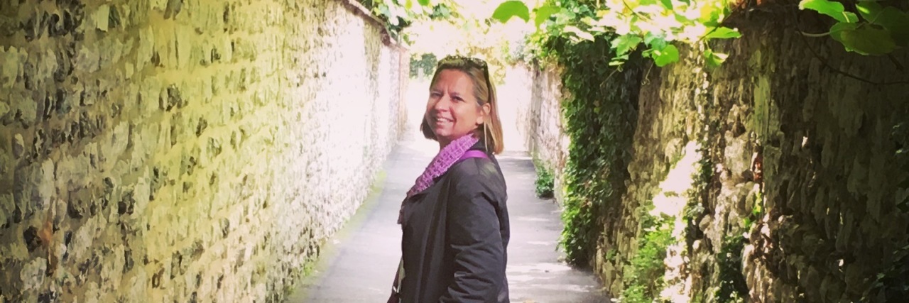 My Experience With Perimenopause woman standing in an outdoor corridor with stone walls and a ceiling covered with leaves