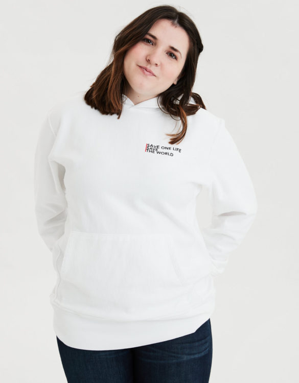 Young woman wearing a white hoodie that says 'save one life, save the world' on it against a white backdrop