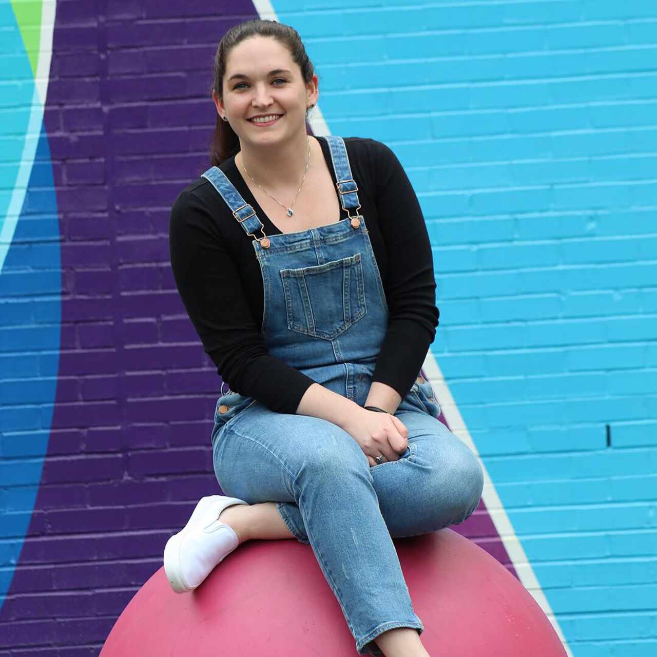 Abigail wearing overalls, sitting outside on a pink ball.