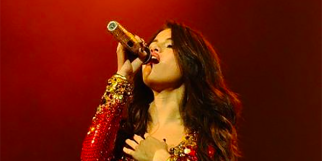 Selena Gomez singing while wearing a red sparkly drress