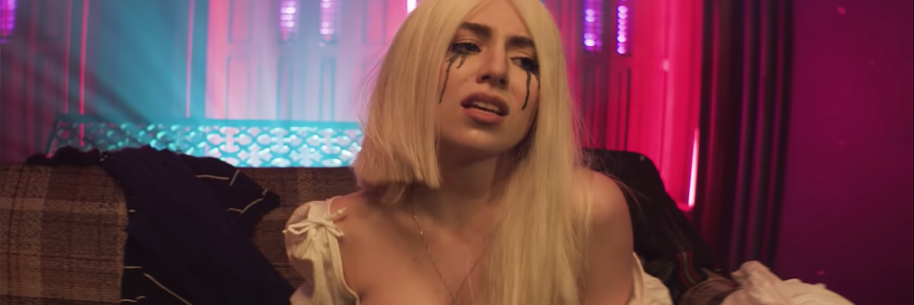 photo from Ava Max video for Sweet but Psycho showing blonde woman with black makeup running from eyes like tears