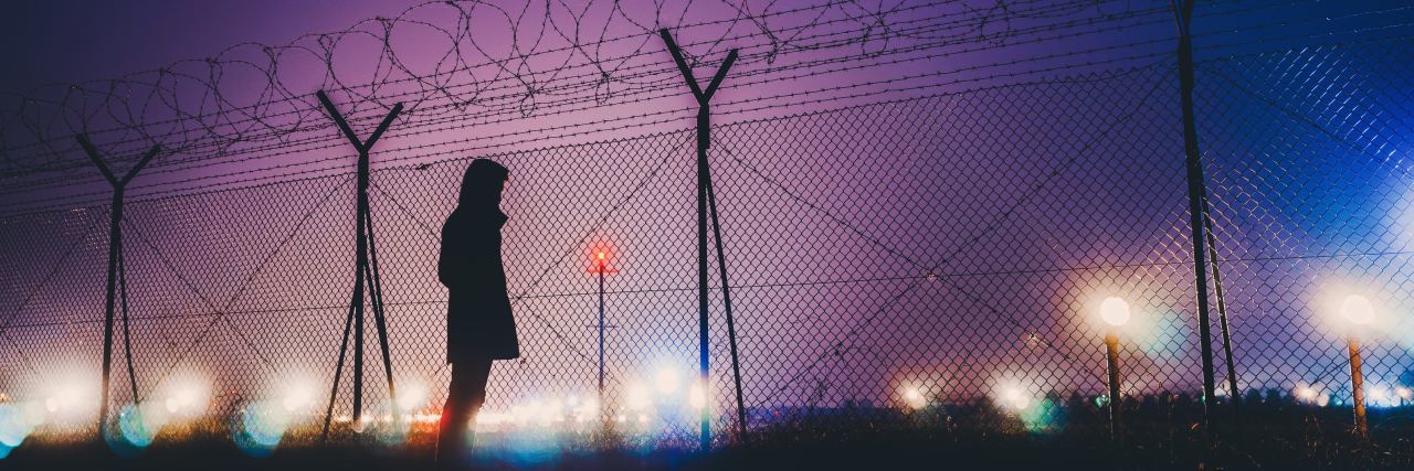 photo of woman silhouetted standing by airport fence at night