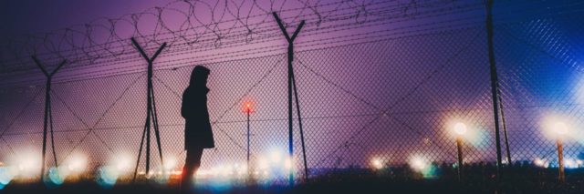 photo of woman silhouetted standing by airport fence at night