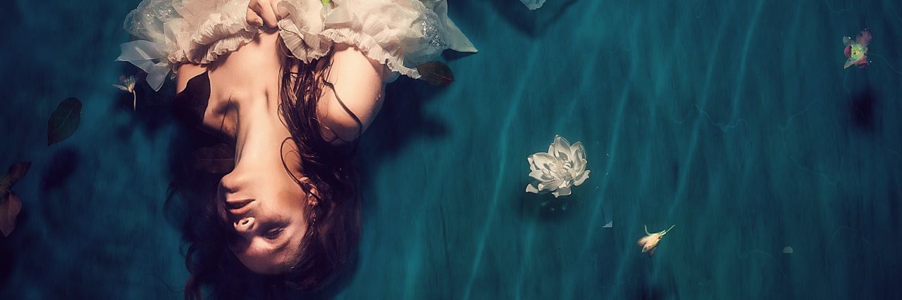 photo of woman in white dress lying in water looking up