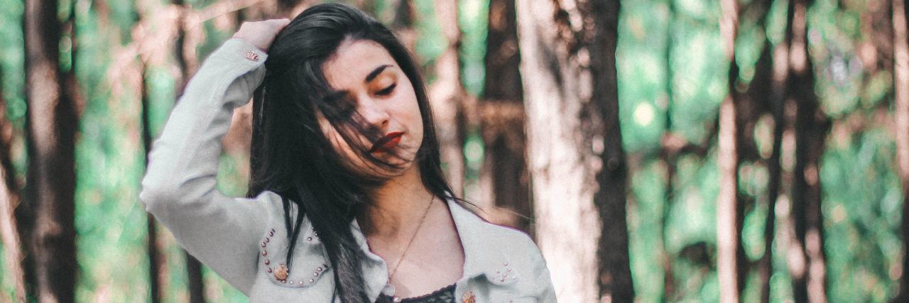 Surprising Symptoms of a Traumatic Brain Injury photo of woman with dark hair in forest with her hand in hair