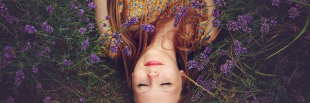 overhead photo of woman lying in purple flowers with eyes closed and smiling